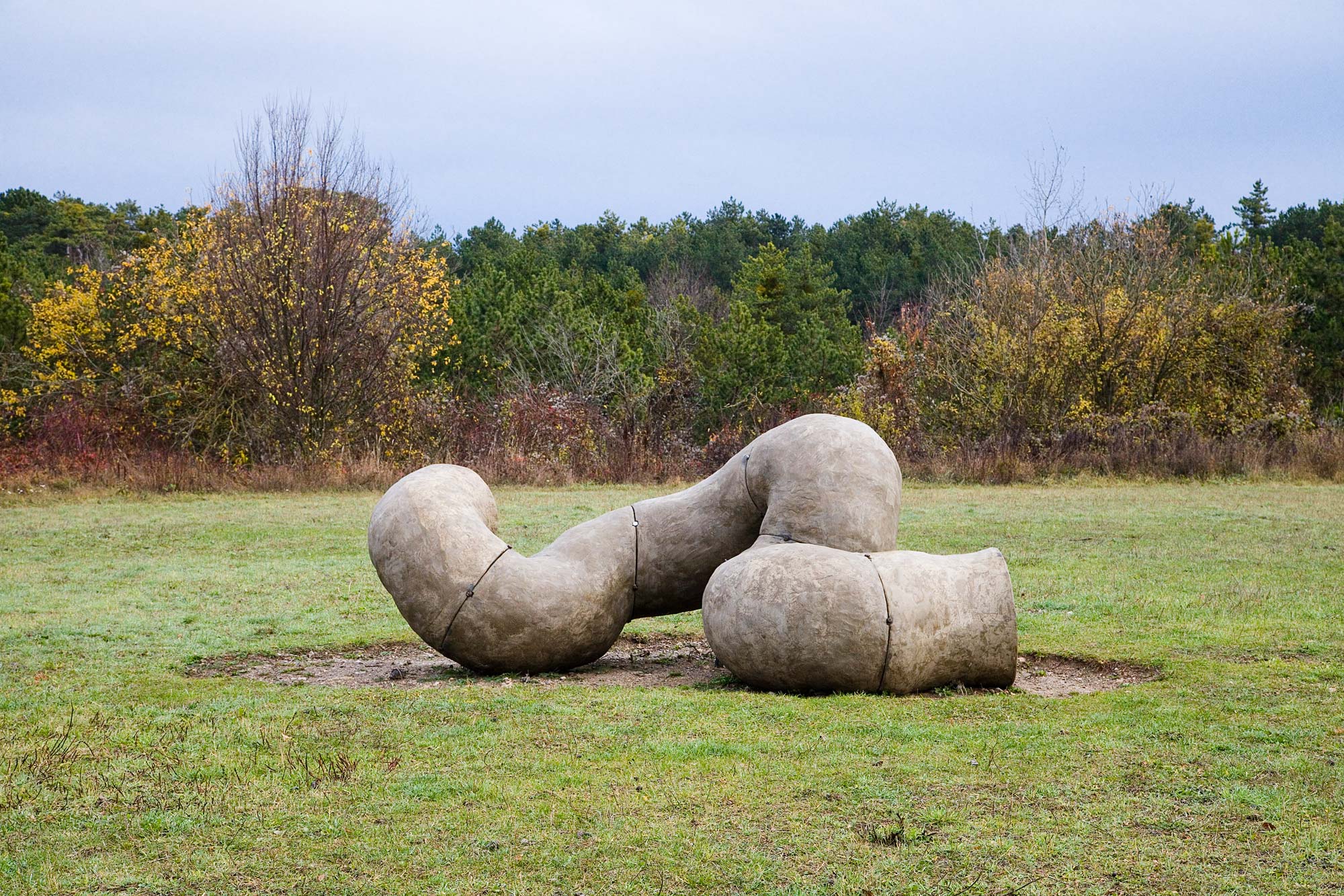 An winding wormhole performance sculpture made of concrete lies on a grassfield