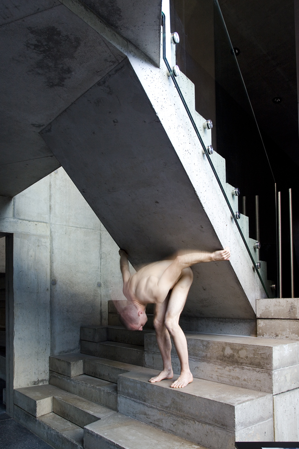 Matthias Mollner stands bent over and naked under a concrete staircase in the Domenig Steinhaus